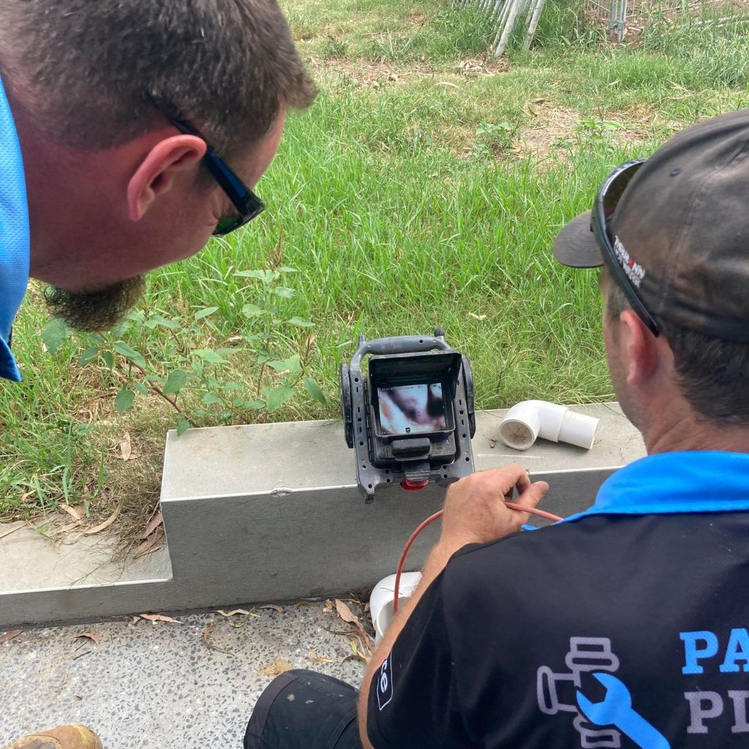 two men looking at a CCTV camera which is inspecting the inside of a drain